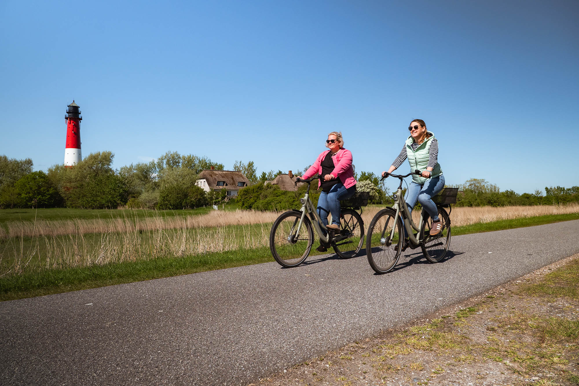 Zwei Frauen fahren mit Fahrrädern am Pellwormer Leuchtturm vorbei