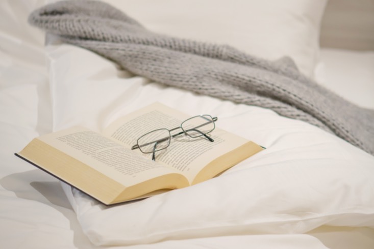 Offenes Buch und Brille auf einem Bett